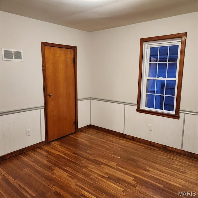 spare room featuring wood finished floors, a wainscoted wall, and baseboards