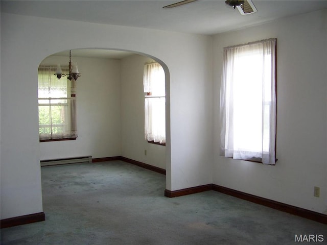 empty room with baseboard heating, plenty of natural light, carpet floors, and arched walkways