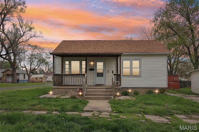 bungalow with covered porch, a shingled roof, and a yard