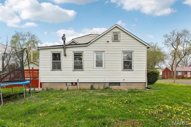 back of property with a trampoline and a yard
