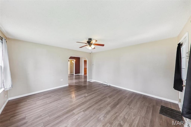 unfurnished room with arched walkways, ceiling fan, wood finished floors, and baseboards