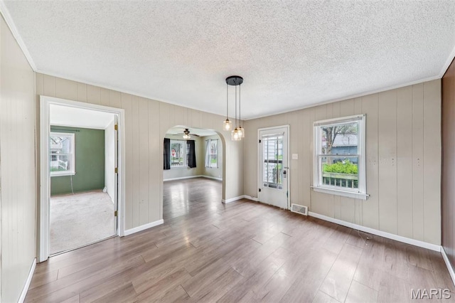 unfurnished dining area with wood finished floors, a textured ceiling, ceiling fan, arched walkways, and baseboards