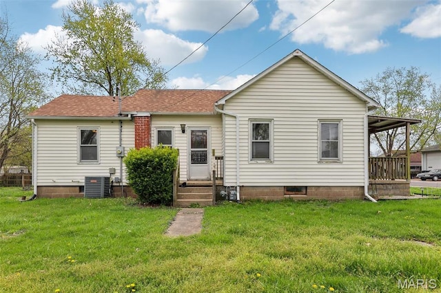 rear view of property featuring central AC unit, a yard, and a shingled roof