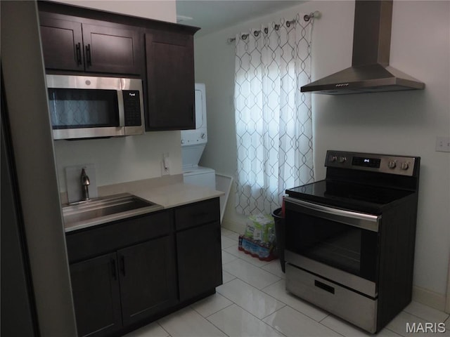 6518 Chamberlain Ave, Saint Louis, MO 63130 - kitchen featuring stainless steel appliances, wall chimney exhaust hood, stacked washer and clothes dryer, a sink, and light countertops