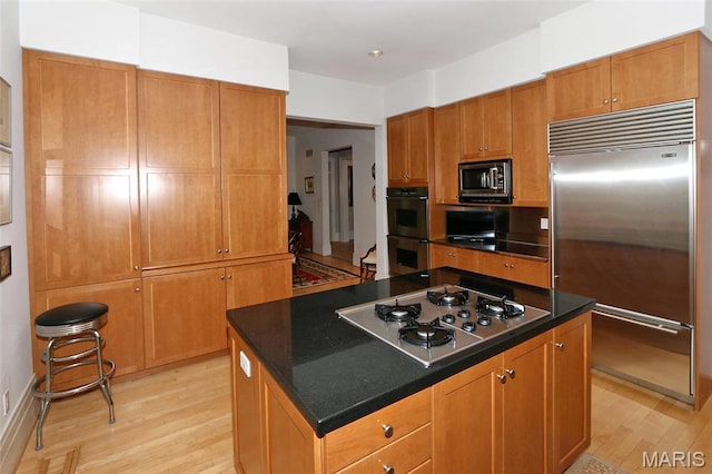 7788 Pershing Ave, Clayton, MO 63105 - kitchen featuring appliances with stainless steel finishes, light wood-type flooring, a kitchen island, and dark countertops