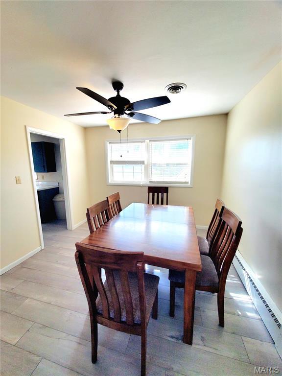 dining space featuring baseboard heating, a ceiling fan, baseboards, and light wood finished floors