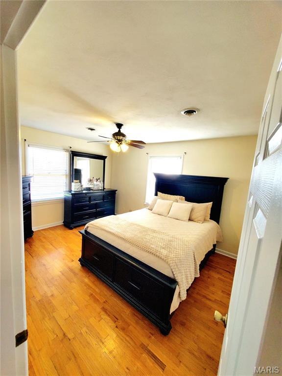 bedroom with light wood-type flooring, multiple windows, baseboards, and ceiling fan