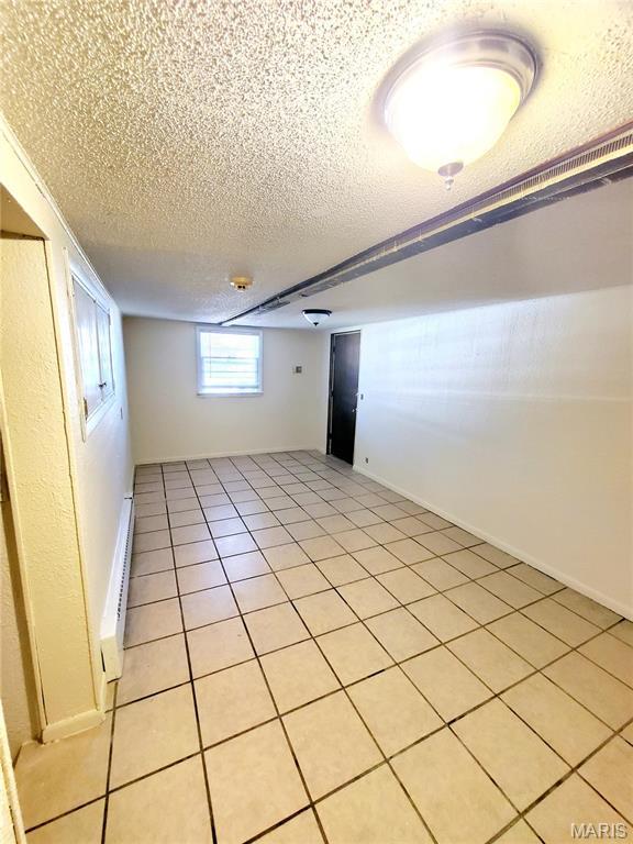 basement featuring a baseboard radiator, a textured ceiling, and light tile patterned floors