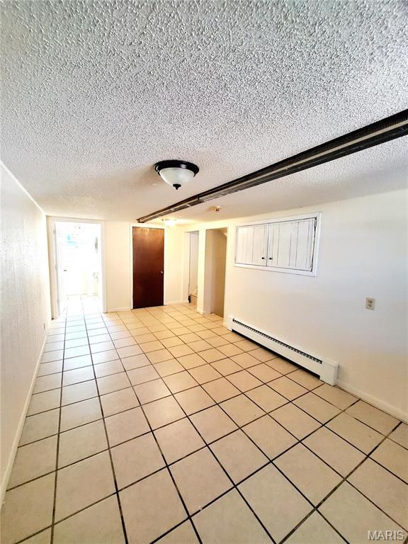 empty room with baseboard heating, a textured ceiling, light tile patterned flooring, and baseboards