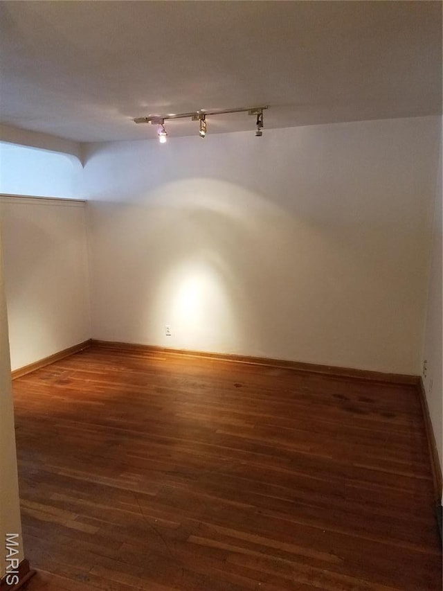 spare room with rail lighting, wood finished floors, and baseboards