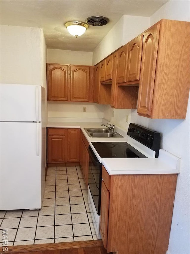 kitchen featuring freestanding refrigerator, electric stove, a sink, light tile patterned floors, and light countertops