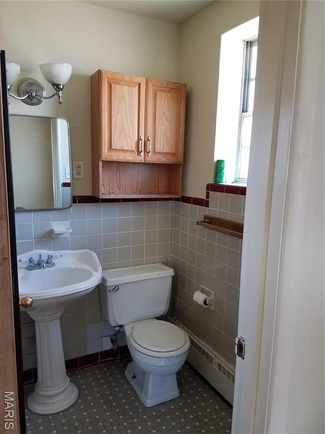 bathroom with a baseboard heating unit, tile walls, toilet, tile patterned flooring, and a wainscoted wall
