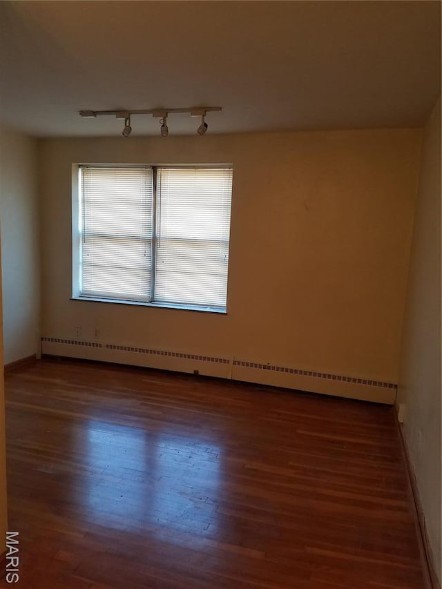 unfurnished room featuring wood finished floors, a baseboard heating unit, and baseboards