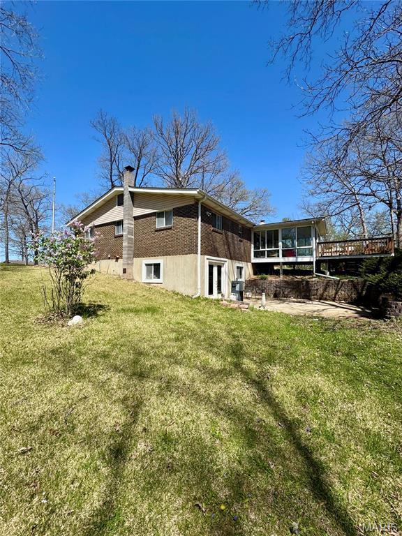 back of house featuring a sunroom, french doors, a yard, a chimney, and brick siding