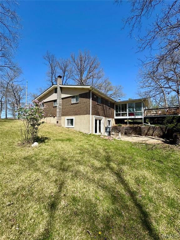 back of house featuring a sunroom, a chimney, a yard, brick siding, and french doors