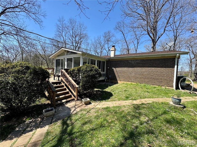 view of front of home with a sunroom, a chimney, brick siding, a front yard, and stairs