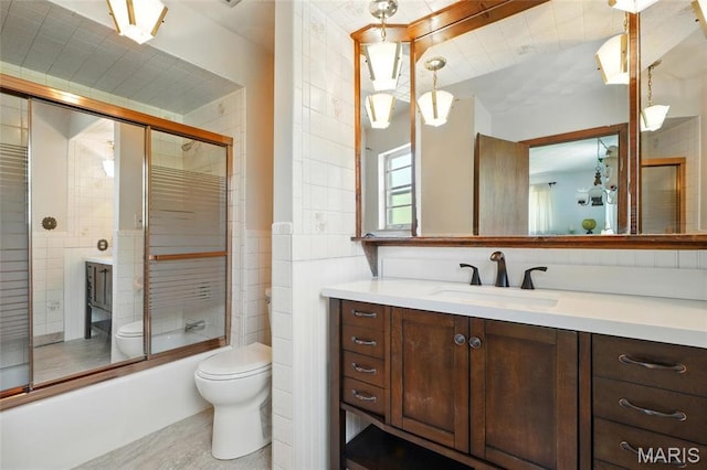 bathroom with toilet, vanity, bath / shower combo with glass door, and tile walls