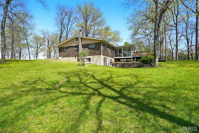 back of house featuring a sunroom, a chimney, a yard, and a wooden deck