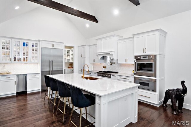 kitchen with appliances with stainless steel finishes, a sink, white cabinetry, beamed ceiling, and backsplash