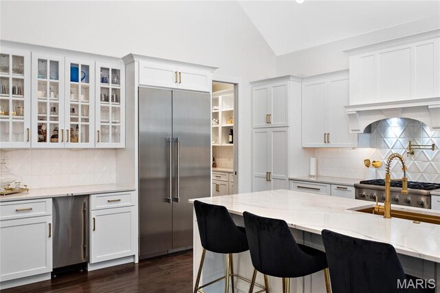 kitchen featuring stainless steel built in fridge, lofted ceiling, tasteful backsplash, glass insert cabinets, and white cabinets