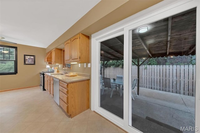 kitchen with appliances with stainless steel finishes, a sink, light countertops, baseboards, and beam ceiling