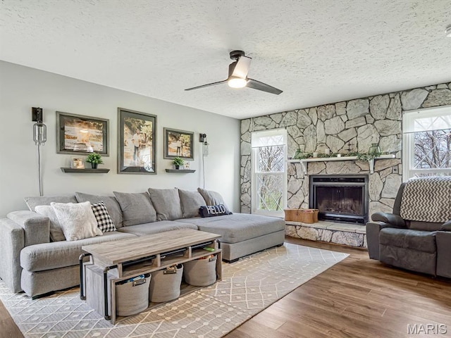 7506 D Rd, Waterloo, IL 62298 - living area with a textured ceiling, wood finished floors, a ceiling fan, and a stone fireplace