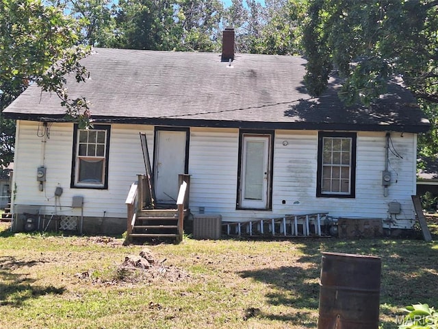 view of front of house with entry steps, a front lawn, a chimney, and central AC