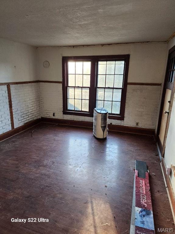 unfurnished room with healthy amount of natural light, concrete flooring, baseboards, a textured ceiling, and brick wall