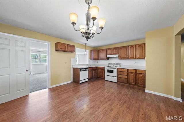 4044 Locke Ave, Bridgeton, MO 63044 - kitchen with white appliances, under cabinet range hood, brown cabinets, a chandelier, and light countertops