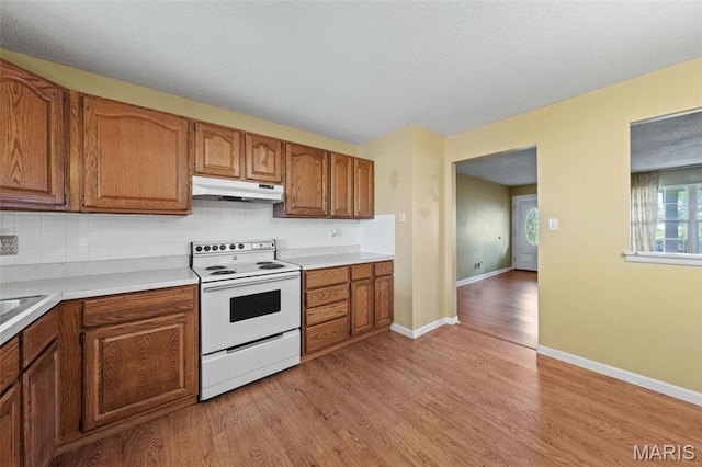 4044 Locke Ave, Bridgeton, MO 63044 - kitchen with white electric stove, under cabinet range hood, light wood-style flooring, and brown cabinets