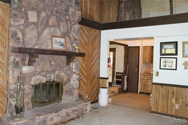 unfurnished living room with wooden walls, unfinished concrete flooring, a fireplace, and a wainscoted wall