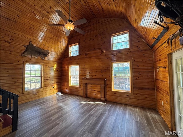 unfurnished living room with high vaulted ceiling, wooden ceiling, wood walls, wood finished floors, and a ceiling fan
