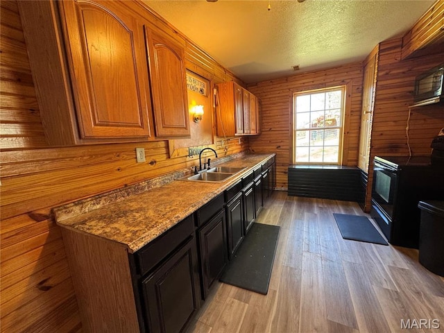 kitchen featuring a sink, black range with electric cooktop, light wood-type flooring, brown cabinetry, and a textured ceiling