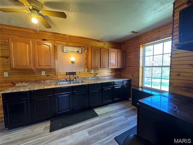 kitchen featuring a sink, a textured ceiling, wooden walls, a ceiling fan, and light wood-type flooring