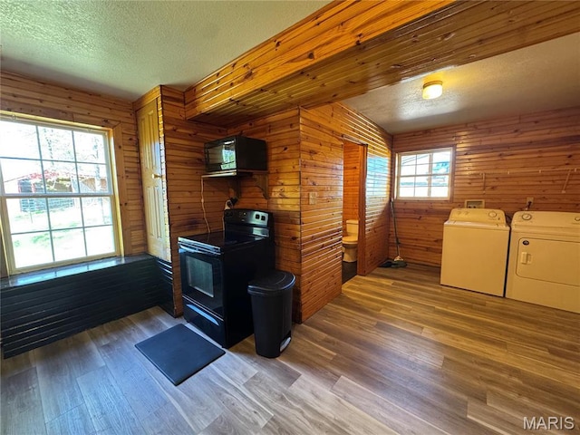 kitchen featuring black appliances, washer and dryer, a textured ceiling, wood finished floors, and a wood stove