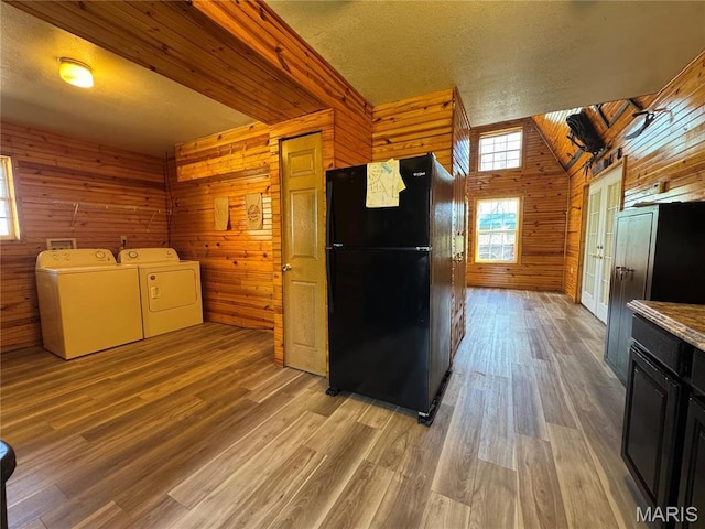 kitchen featuring freestanding refrigerator, wood walls, washer and dryer, light wood-style floors, and vaulted ceiling