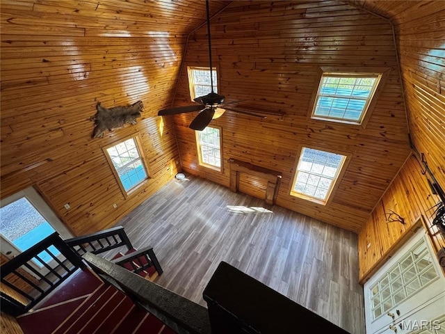 unfurnished living room with high vaulted ceiling, wooden walls, healthy amount of natural light, wood ceiling, and a ceiling fan