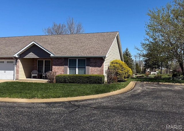 view of front of property featuring brick siding, an attached garage, a shingled roof, and a front lawn