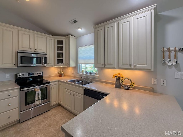 kitchen featuring stainless steel appliances, a sink, lofted ceiling, glass insert cabinets, and light countertops