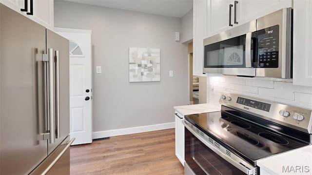 5714 Rhodes Ave, Saint Louis, MO 63109 - kitchen featuring stainless steel appliances, light wood-style flooring, decorative backsplash, white cabinets, and baseboards