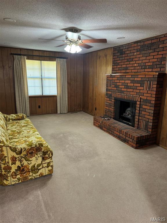 2925 Wayne Ave, Poplar Bluff, MO 63901 - living room with carpet flooring, wood walls, a brick fireplace, a textured ceiling, and a ceiling fan