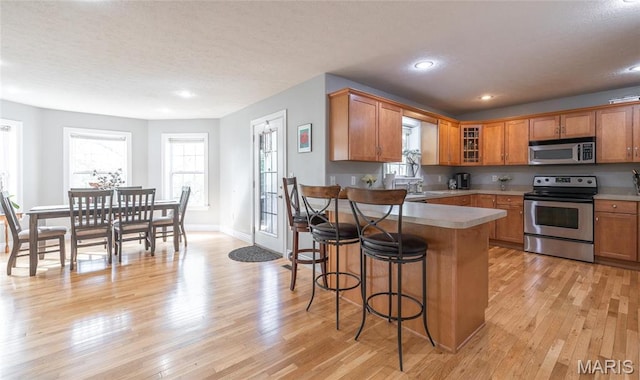 21438 Lancaster Ln, Waynesville, MO 65583 - kitchen featuring stainless steel appliances, a breakfast bar, light wood-type flooring, glass insert cabinets, and recessed lighting