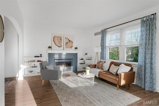 living room featuring wood finished floors, a brick fireplace, arched walkways, and baseboards