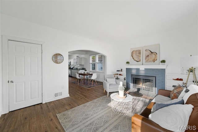 living room featuring arched walkways, wood finished floors, a brick fireplace, and baseboards