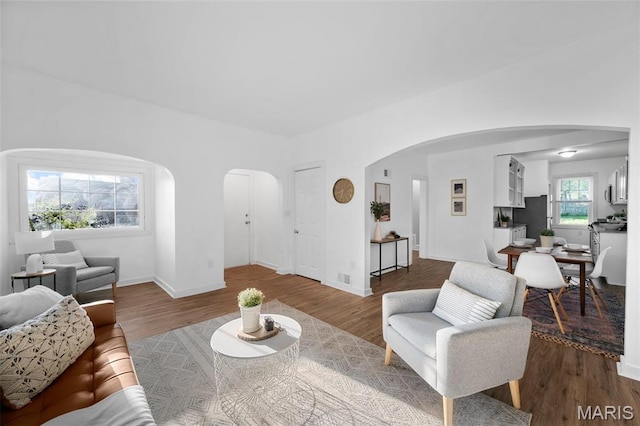 living room with arched walkways, wood finished floors, and baseboards