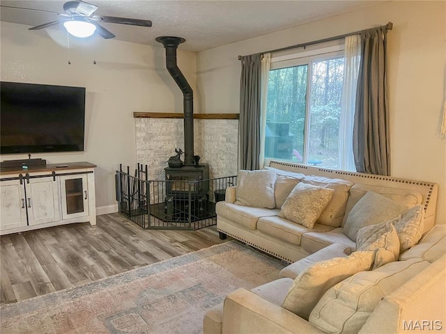 living area featuring a wood stove, a ceiling fan, wood finished floors, and baseboards