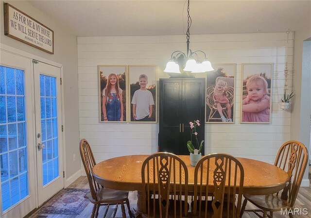 dining area with wood finished floors, wooden walls, a chandelier, and french doors