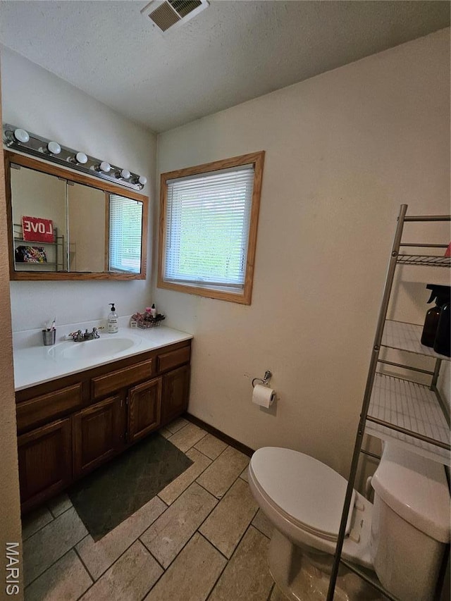 bathroom featuring toilet, vanity, a textured ceiling, and baseboards