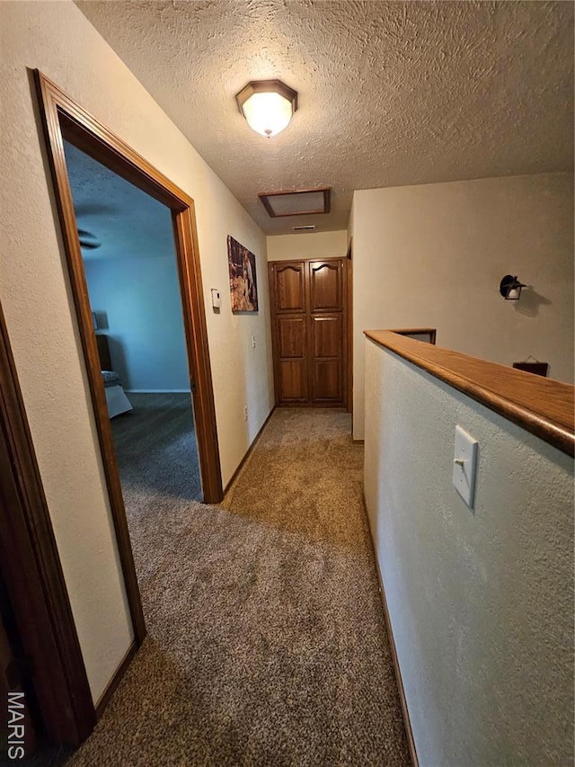 corridor with light carpet, a textured ceiling, an upstairs landing, and attic access