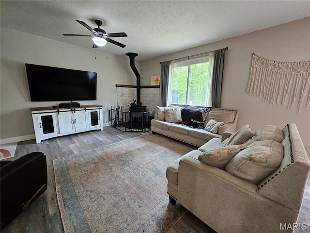 living area featuring a wood stove, wood finished floors, a ceiling fan, a textured ceiling, and baseboards
